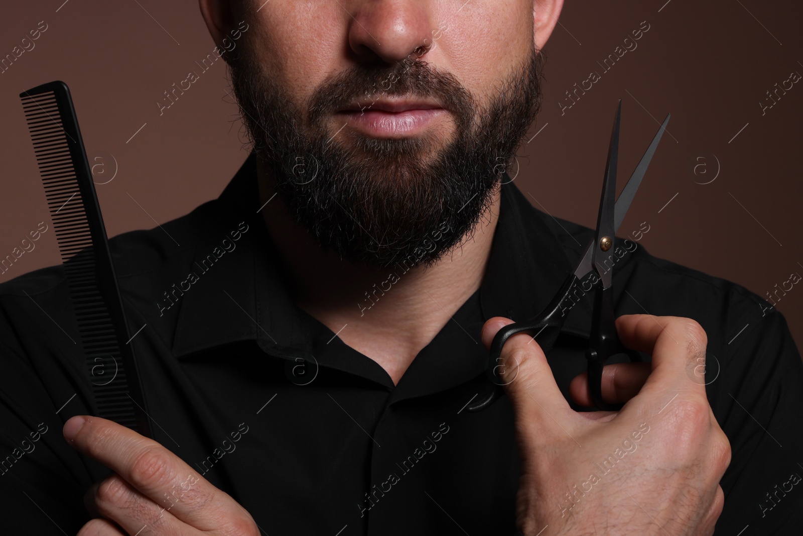 Photo of Bearded man holding comb and scissors on brown background, closeup