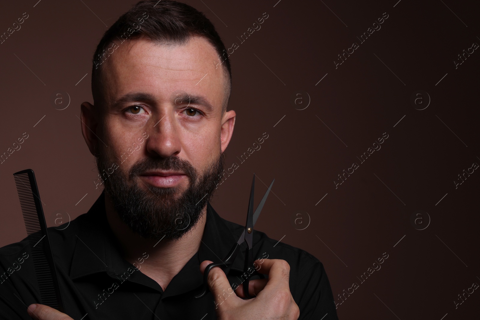 Photo of Bearded man holding comb and scissors on brown background, space for text