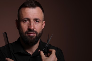 Photo of Bearded man holding comb and scissors on brown background, space for text