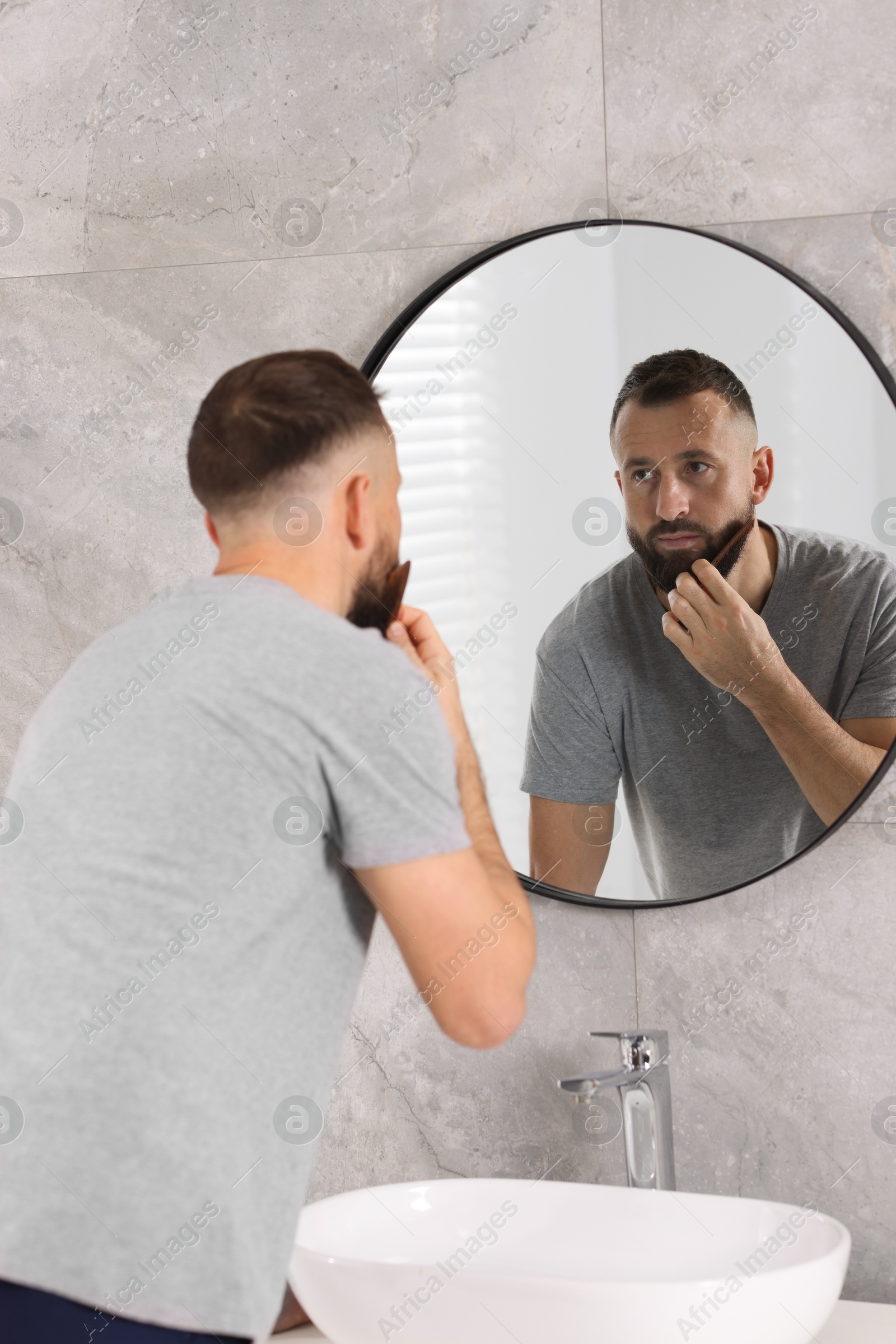 Photo of Man combing beard near mirror in bathroom