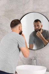 Photo of Man combing beard near mirror in bathroom