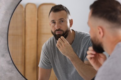 Man combing beard near mirror in bathroom