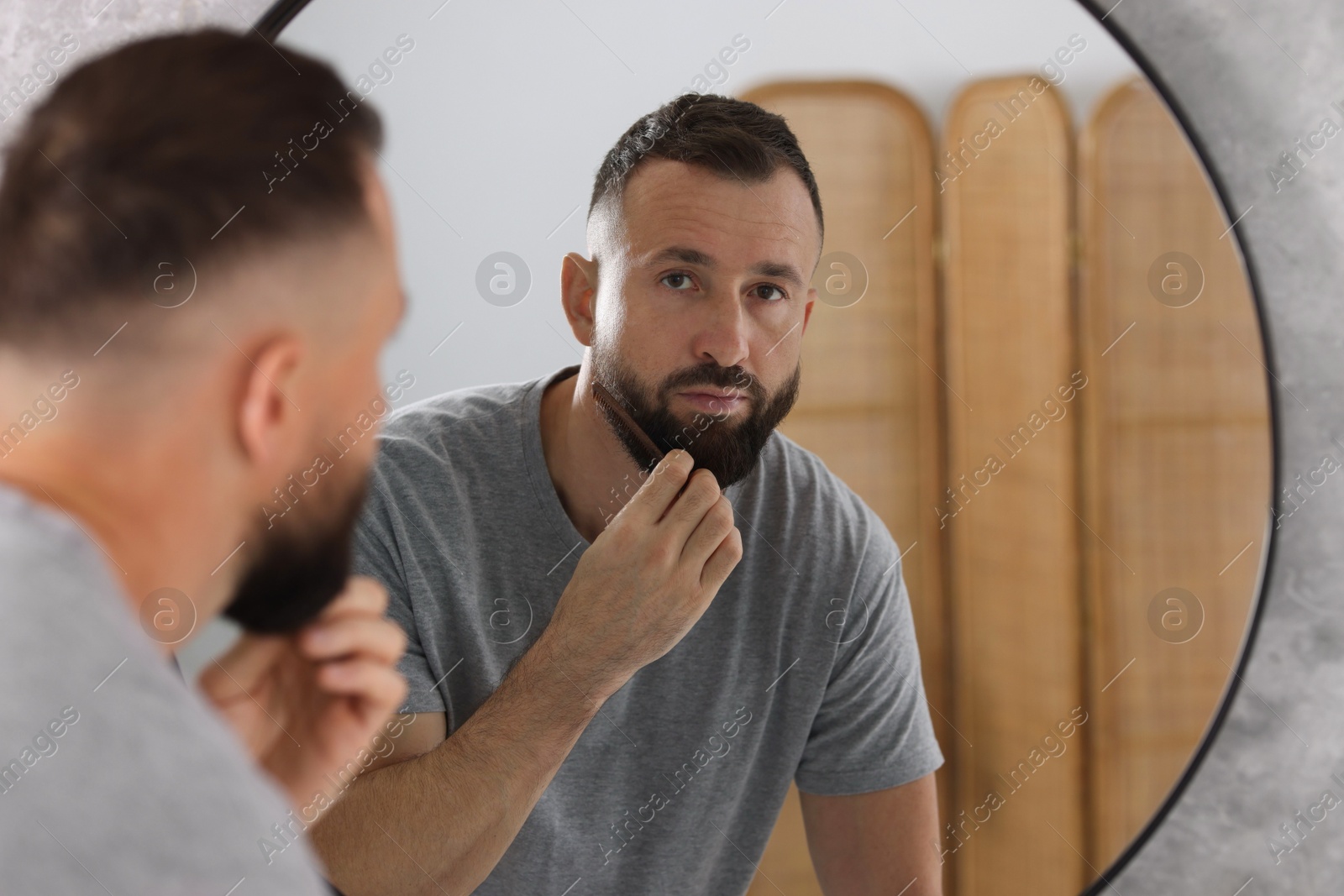 Photo of Man combing beard near mirror in bathroom