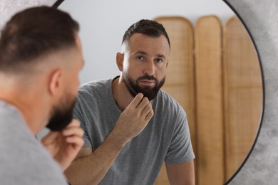 Man combing beard near mirror in bathroom