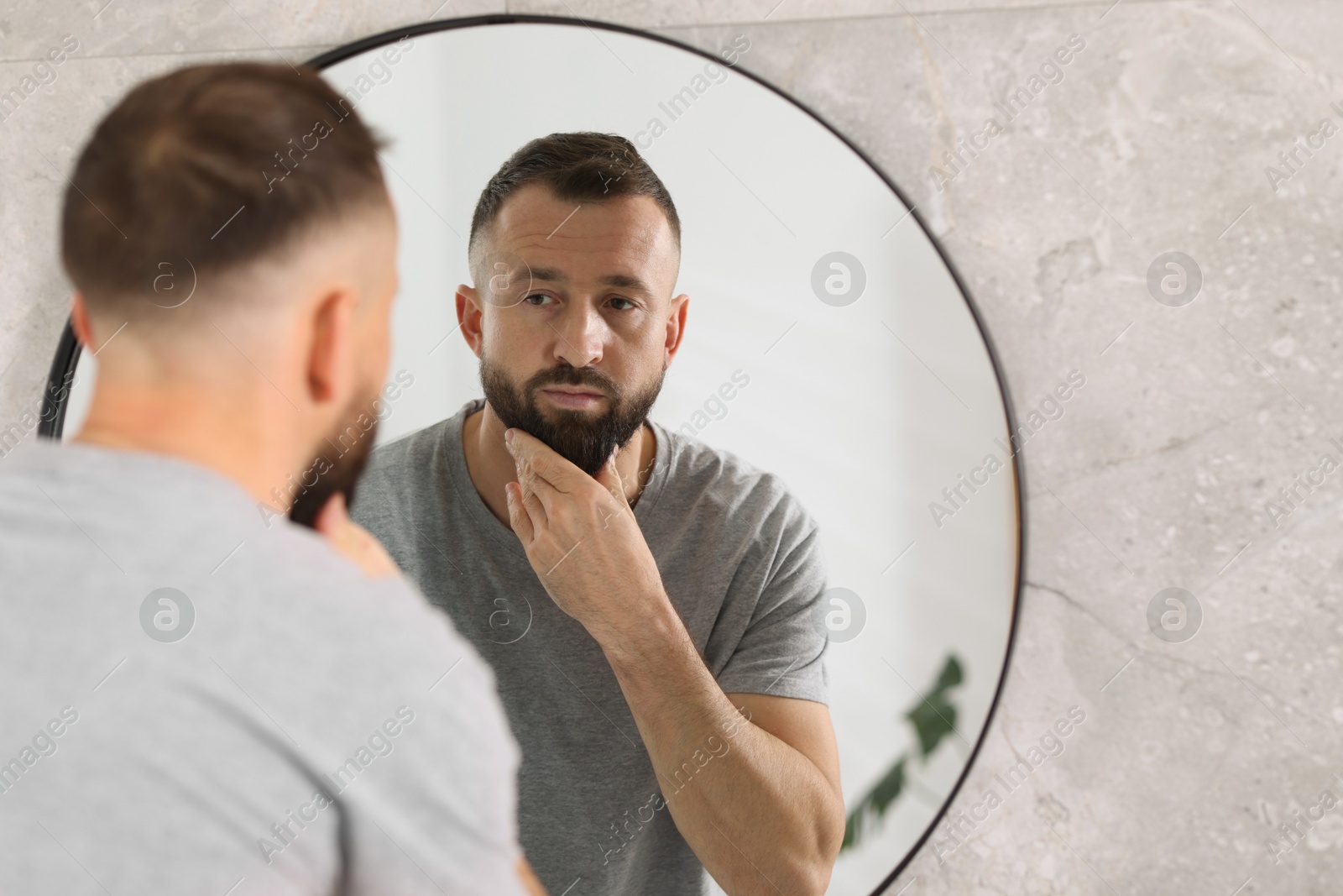 Photo of Handsome bearded man near mirror in bathroom