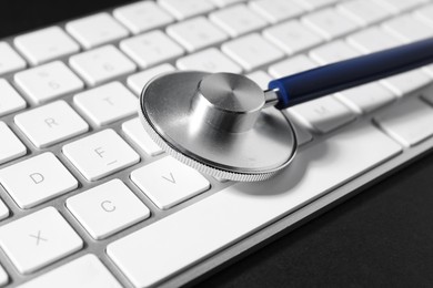 Photo of Technical support concept. Stethoscope and keyboard on black background, closeup