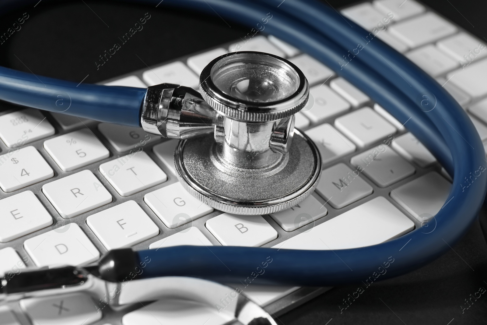 Photo of Technical support concept. Stethoscope and keyboard on black background, closeup