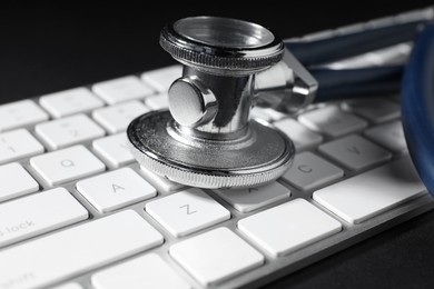 Photo of Technical support concept. Stethoscope and keyboard on black background, closeup