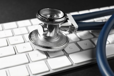 Photo of Technical support concept. Stethoscope and keyboard on black background, closeup