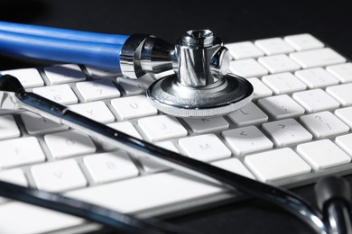 Photo of Technical support concept. Stethoscope and keyboard on black background, closeup