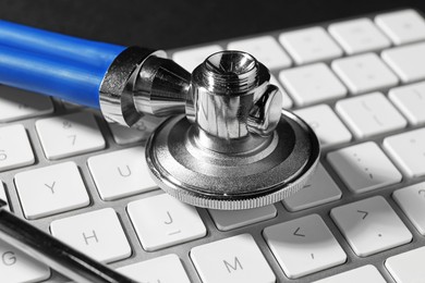 Photo of Technical support concept. Stethoscope and keyboard on black background, closeup