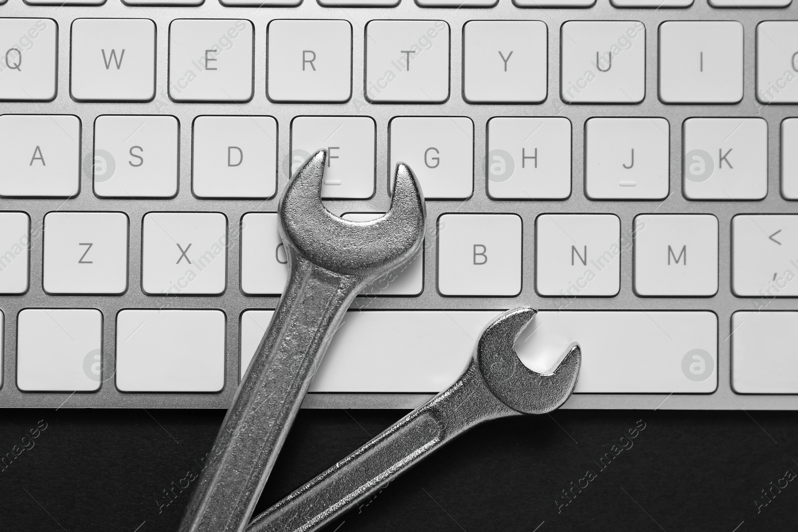 Photo of Technical support concept. Wrenches and keyboard on black background, top view