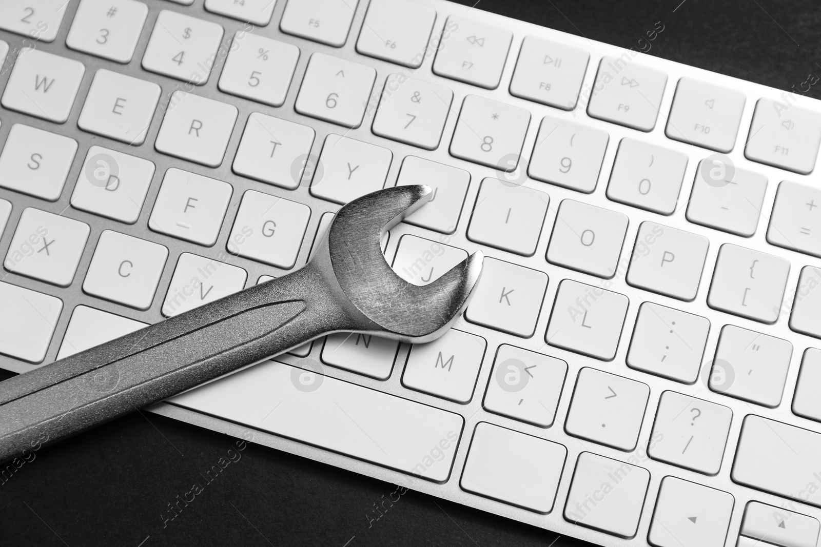 Photo of Technical support concept. Wrench and keyboard on black background, top view