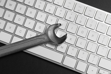 Photo of Technical support concept. Wrench and keyboard on black background, top view