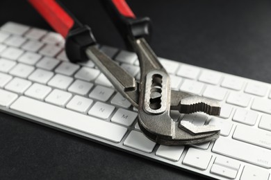 Photo of Technical support concept. Plumbing pliers and keyboard on black background, closeup