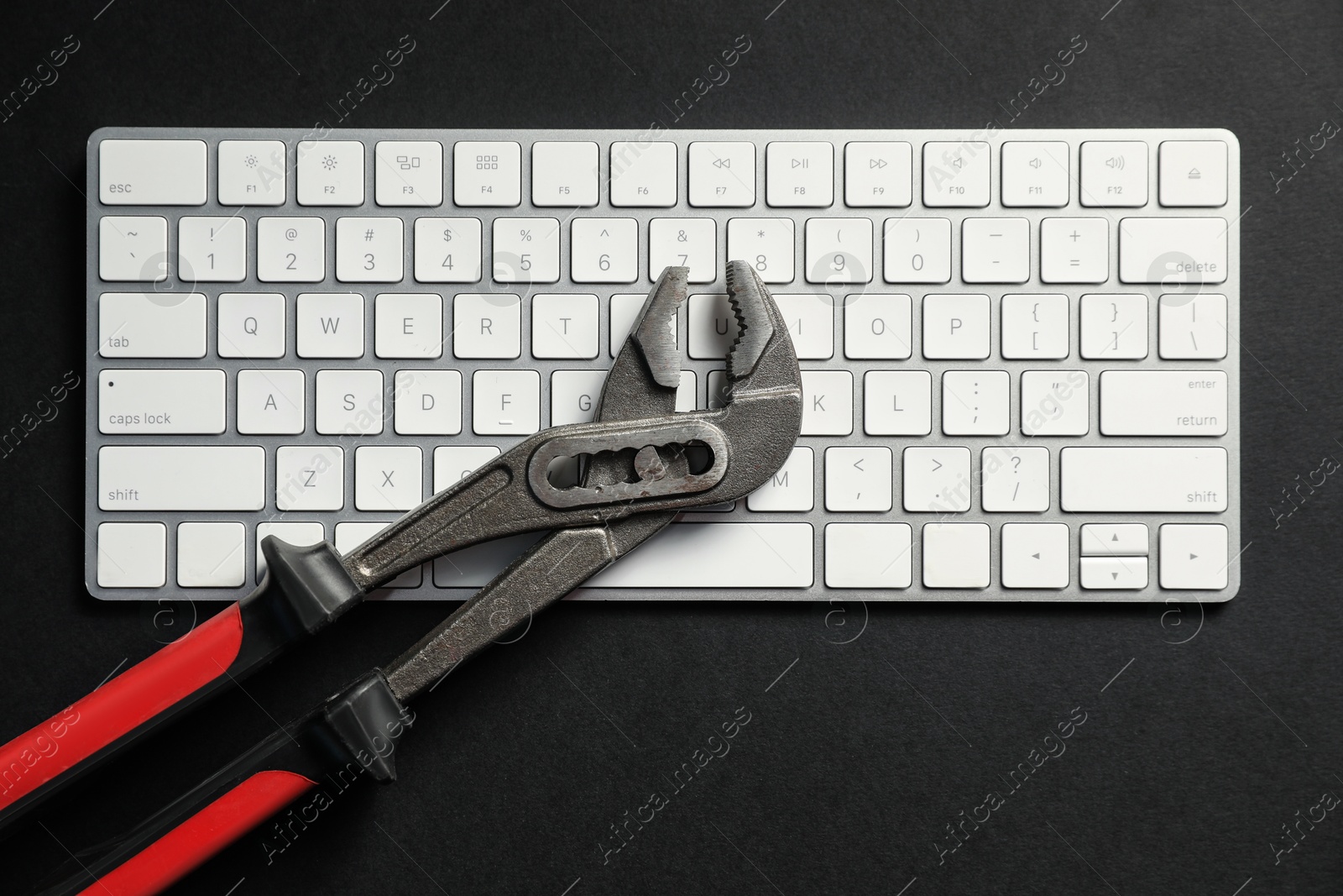 Photo of Technical support concept. Plumbing pliers and keyboard on black background, top view