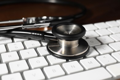 Photo of Technical support concept. Stethoscope and keyboard on wooden table, closeup