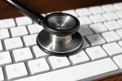 Photo of Technical support concept. Stethoscope and keyboard on wooden table, closeup