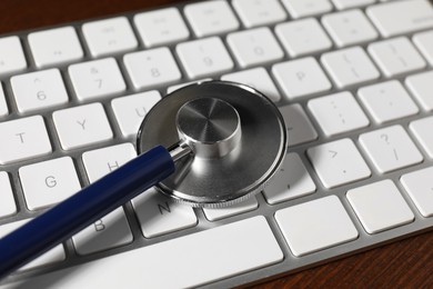 Photo of Technical support concept. Stethoscope and keyboard on wooden table, closeup