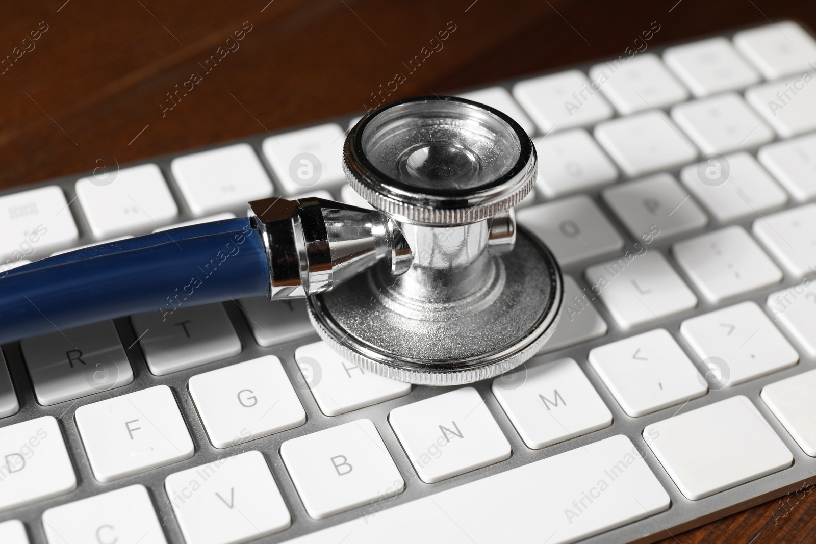 Photo of Technical support concept. Stethoscope and keyboard on wooden table, closeup