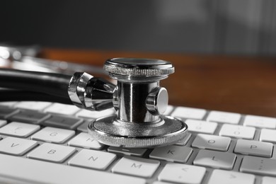 Photo of Technical support concept. Stethoscope and keyboard on wooden table, closeup