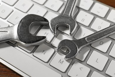 Photo of Technical support concept. Wrenches and keyboard on wooden background, closeup