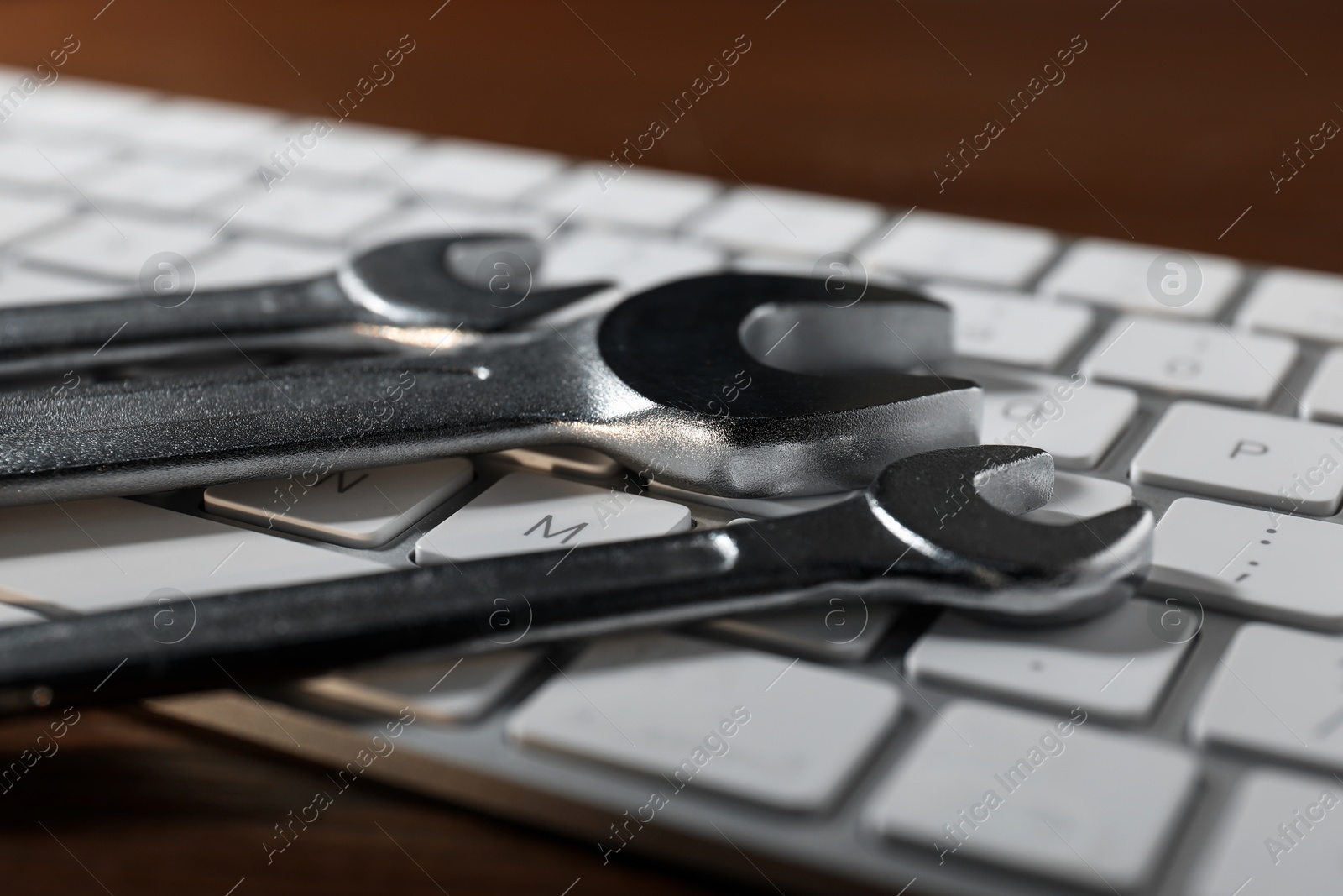 Photo of Technical support concept. Wrenches and keyboard on wooden background, closeup