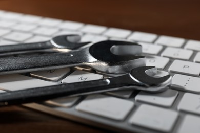 Photo of Technical support concept. Wrenches and keyboard on wooden background, closeup