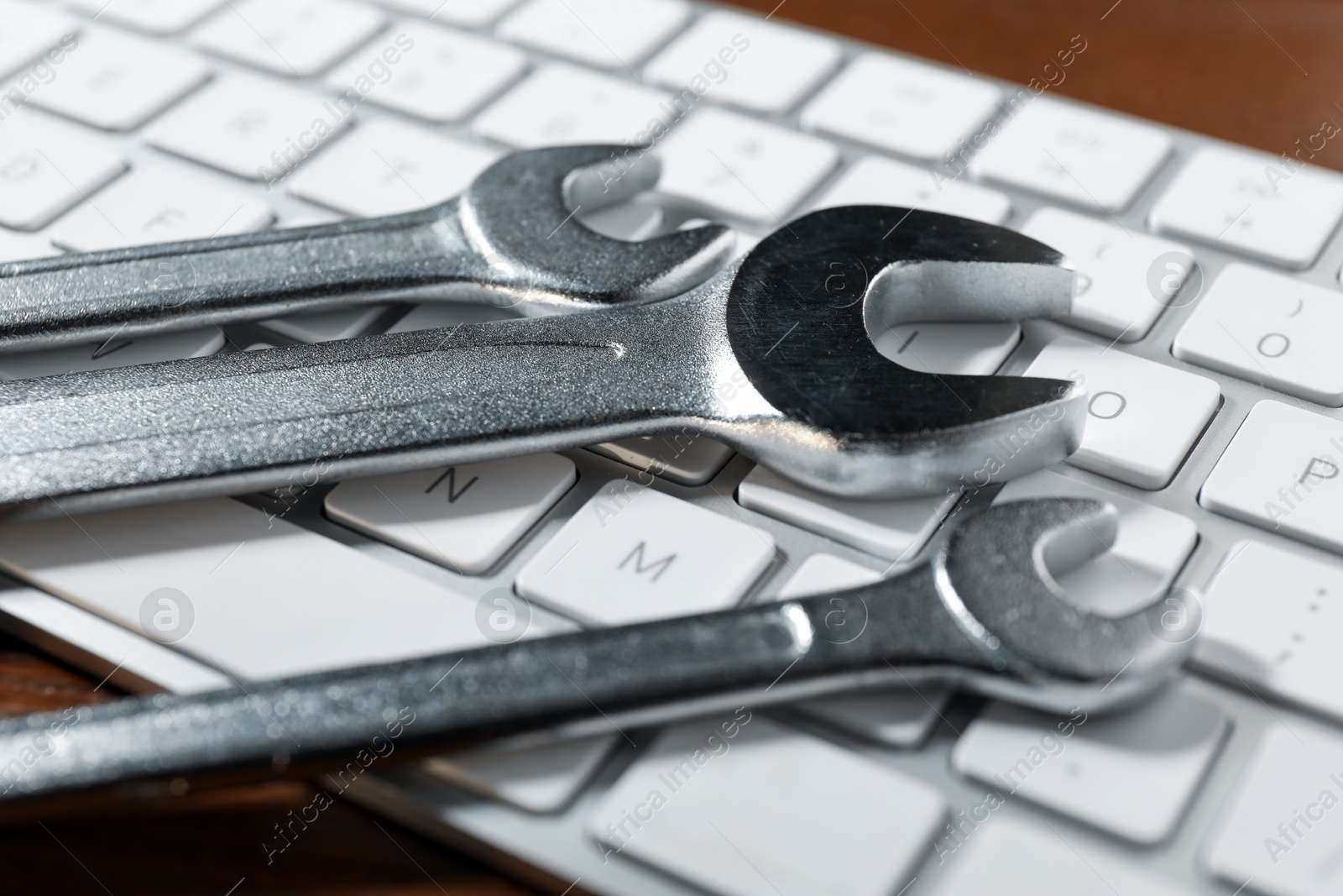 Photo of Technical support concept. Wrenches and keyboard on wooden background, closeup