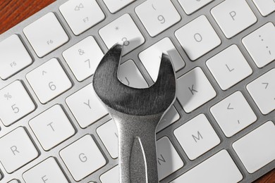 Photo of Technical support concept. Wrench and keyboard on wooden background, top view