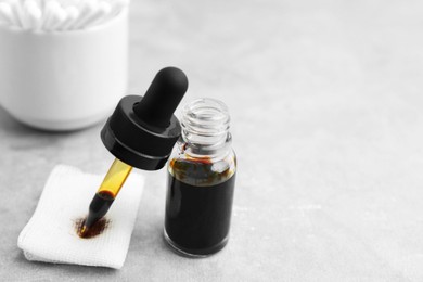 Photo of Bottle of iodine with dropper, piece of bandage and cotton swabs on grey table, closeup. Space for text