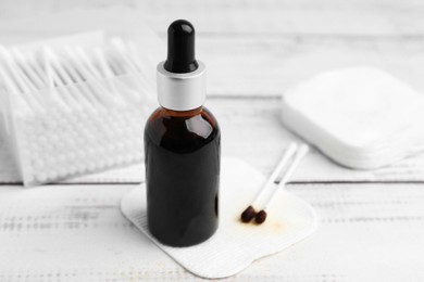 Photo of Bottle of iodine with dropper, cotton pads and swabs on white wooden table, closeup