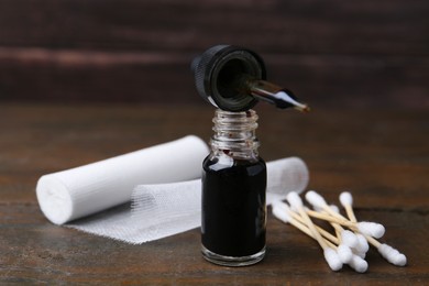 Photo of Bottle of iodine with dropper, cotton swabs and bandage on wooden table, closeup