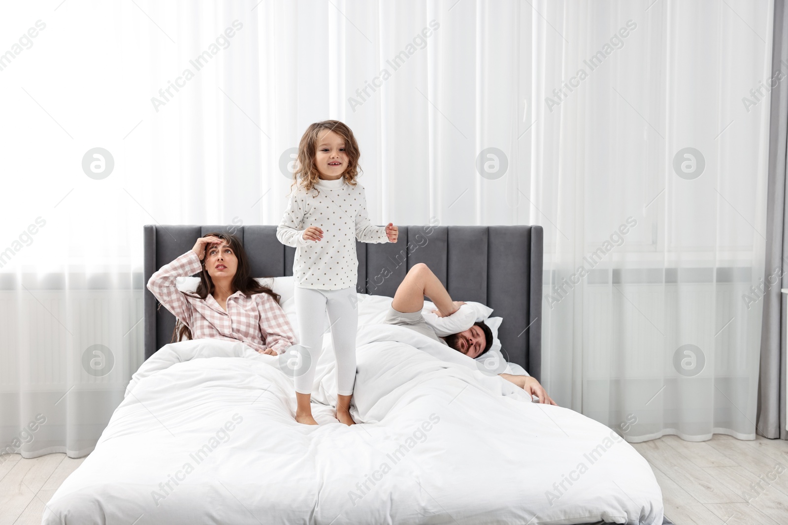 Photo of Happy playful daughter and her overwhelmed parents on bed at home