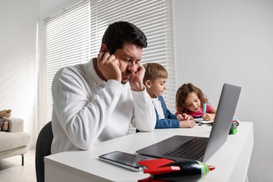 Photo of Naughty children and their overwhelmed father at table with laptop indoors