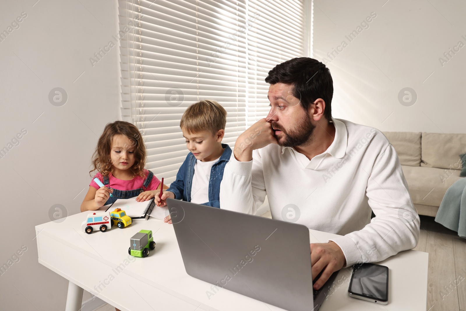 Photo of Naughty children and their overwhelmed father at table with laptop indoors