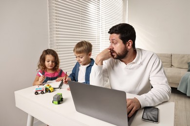 Photo of Naughty children and their overwhelmed father at table with laptop indoors