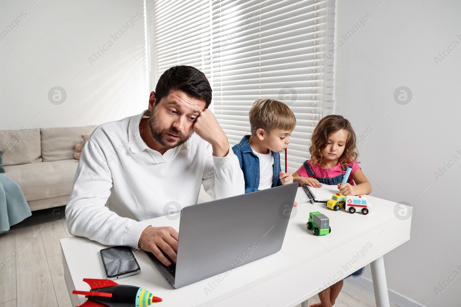 Photo of Naughty children and their overwhelmed father at table with laptop indoors