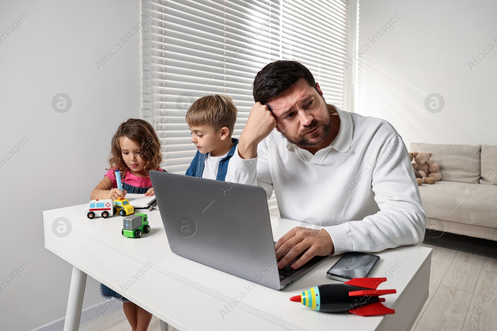 Photo of Naughty children and their overwhelmed father at table with laptop indoors