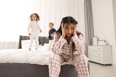 Photo of Overwhelmed mother and her playful children on bed at home