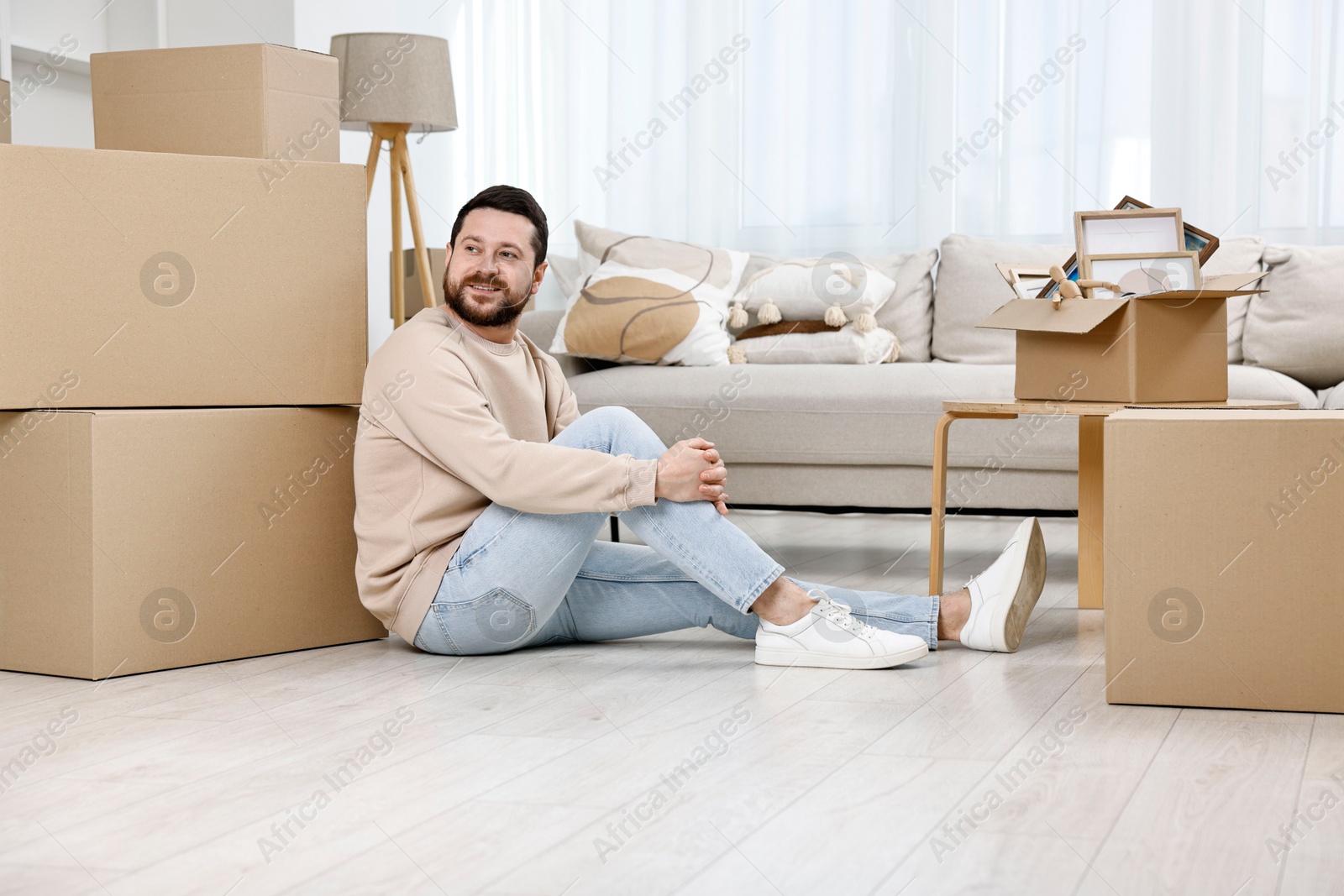 Photo of Moving day. Man resting on floor near cardboard boxes in his new home