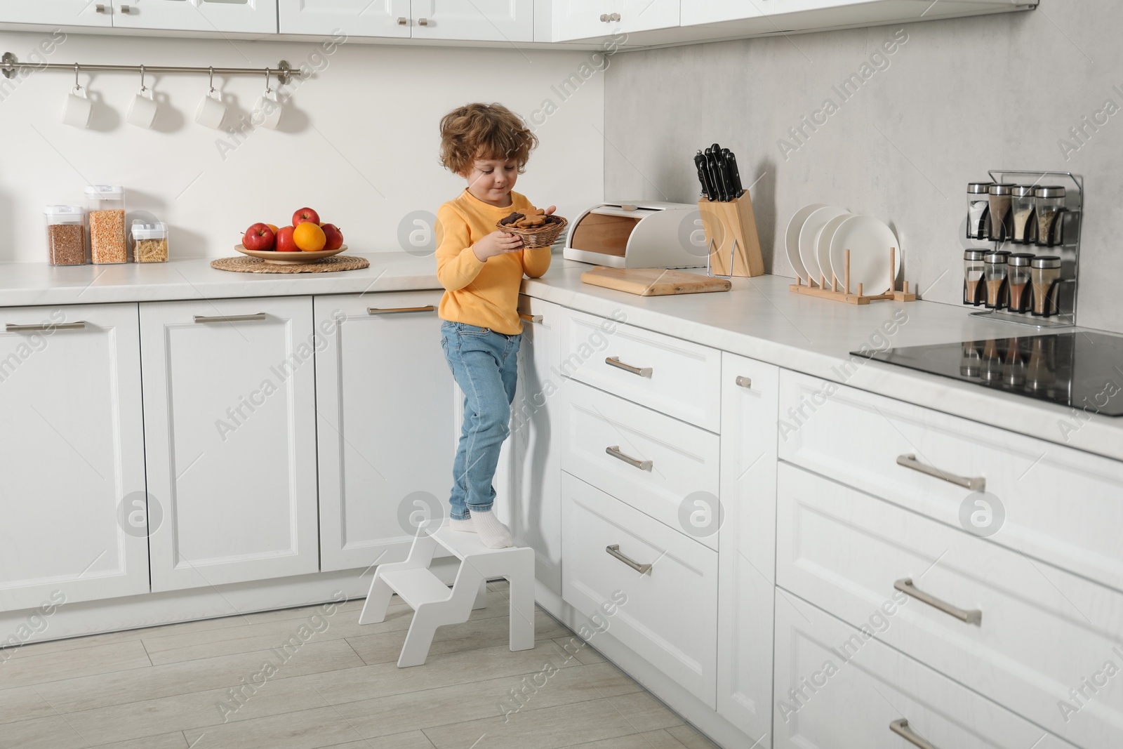 Photo of Little boy with cookies standing on step stool in kitchen