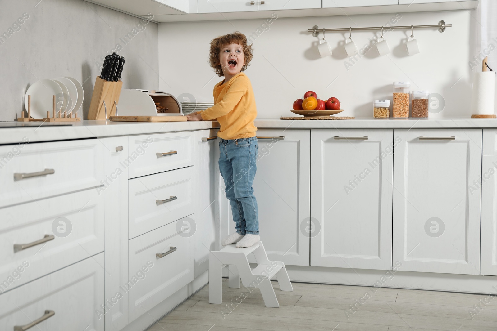 Photo of Little boy standing on step stool near countertop in kitchen