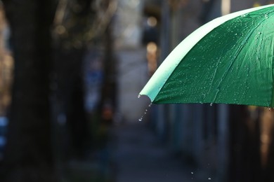 Photo of Open green umbrella under pouring rain outdoors, closeup. Space for text