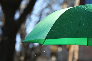 Photo of Open green umbrella under pouring rain outdoors, closeup