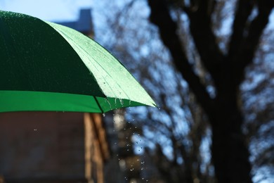 Photo of Open green umbrella under pouring rain outdoors, closeup. Space for text