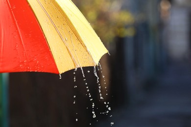 Photo of Open bright umbrella under pouring rain outdoors, closeup. Space for text