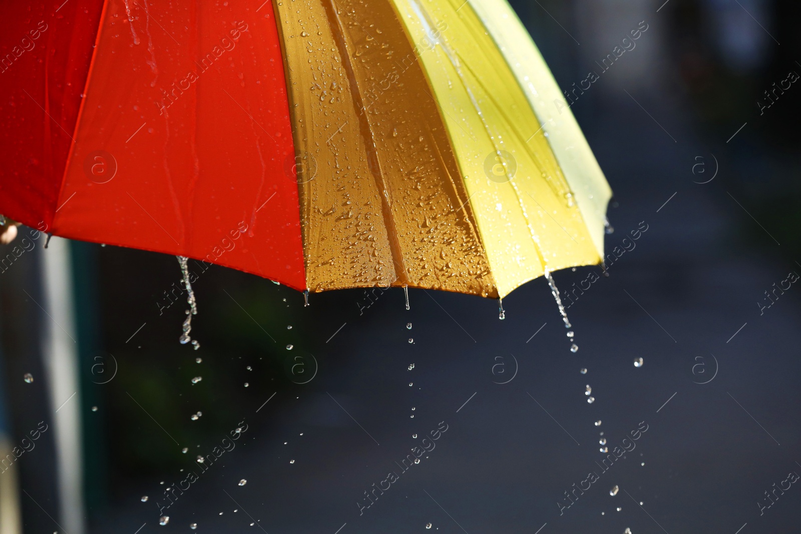 Photo of Open bright umbrella under pouring rain outdoors, closeup