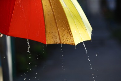 Photo of Open bright umbrella under pouring rain outdoors, closeup