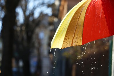 Photo of Open bright umbrella under pouring rain outdoors, closeup. Space for text